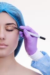 ragazza che si sottoporrà ad intervente do blefaroplastica e cirurgo che traccia le linee intorno agli occhi