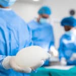 chirurgo che tiene in mano una protesi per mastoplastica prima di operare la paziente