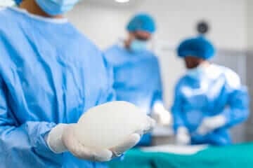 chirurgo che tiene in mano una protesi per mastoplastica prima di operare la paziente